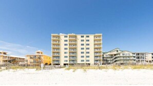 Un hotel de varios pisos con balcones, situado en una playa de arena.