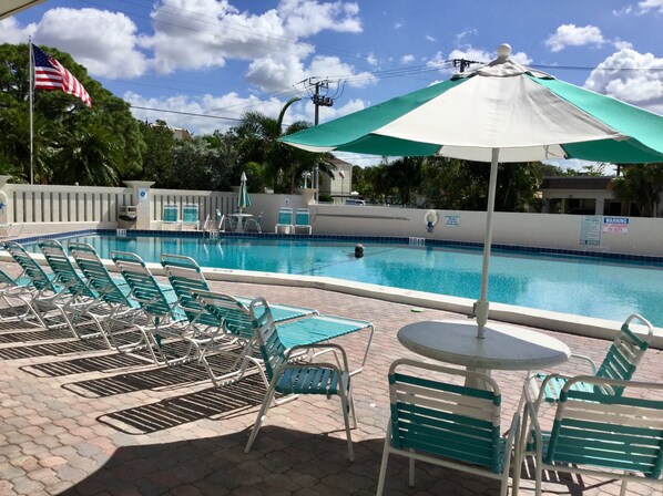 Una piscina con sillas de descanso y una mesa, rodeada por una valla y árboles.