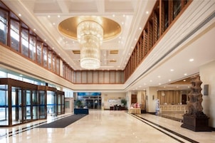 A spacious lobby with a grand chandelier, a reception desk, and a large window.