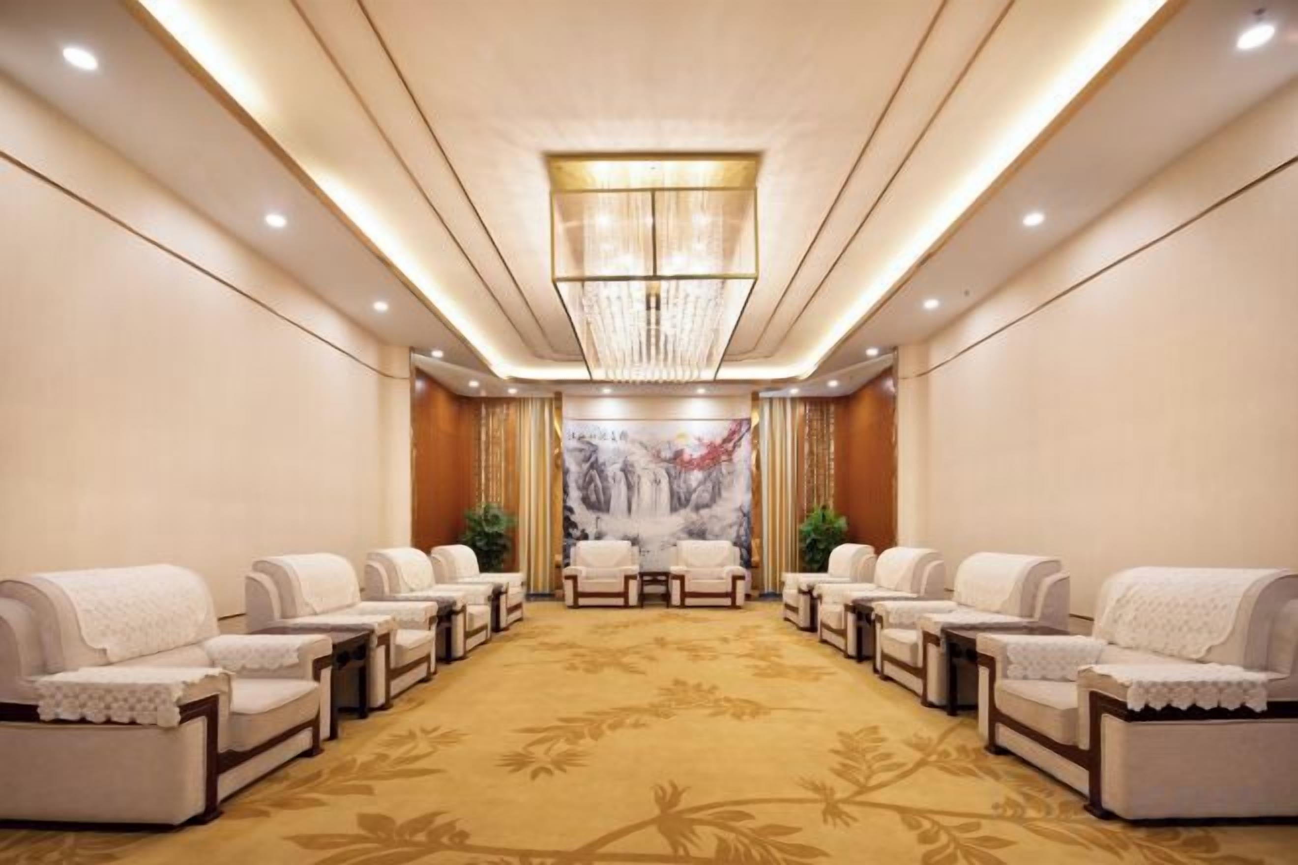 A hotel room with a large carpeted area, multiple seating options, and a chandelier.