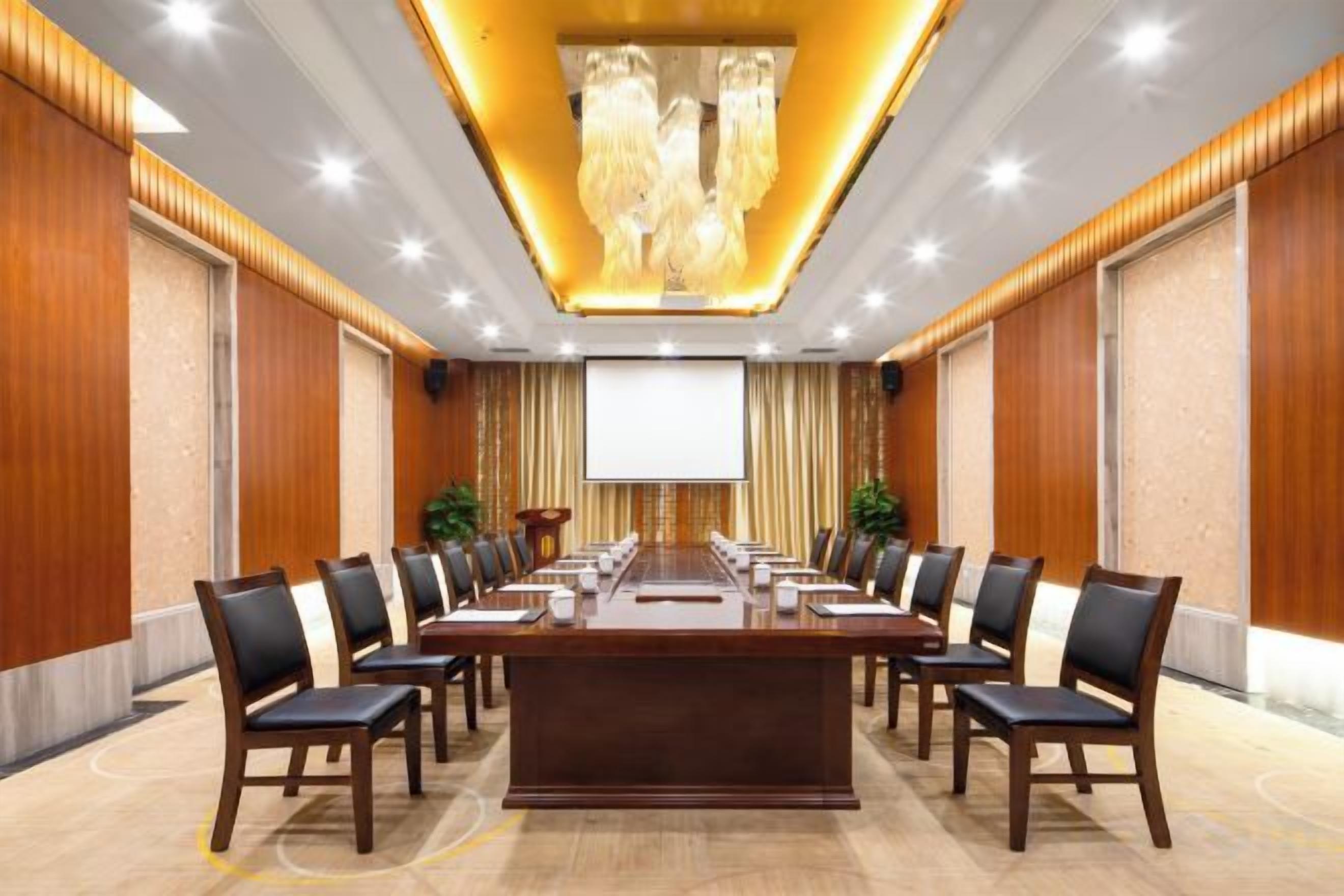 A conference room with a long table, chairs, and a projector screen.