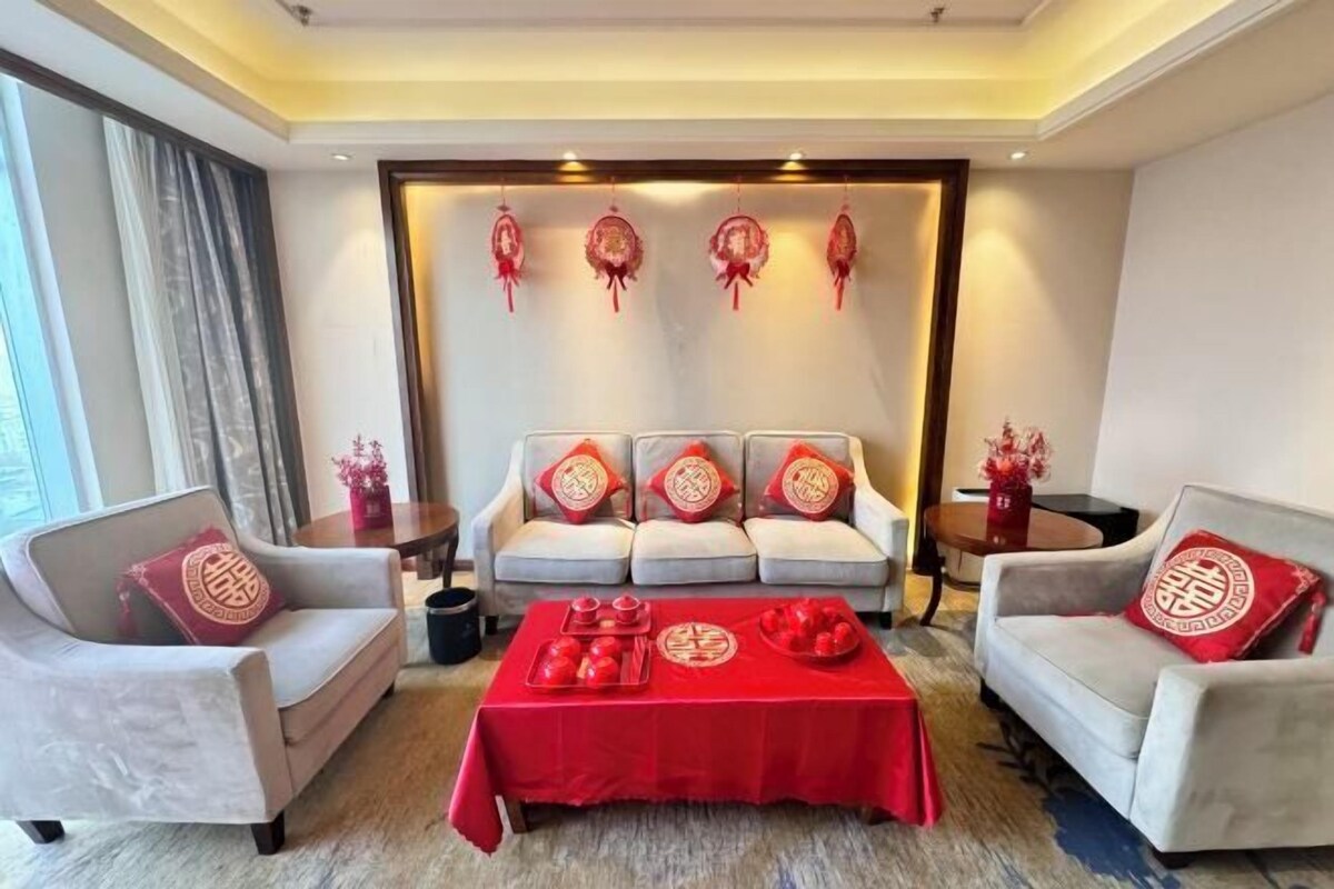 A living room with a sofa set, a coffee table with red tablecloth, and decorative items on the wall.