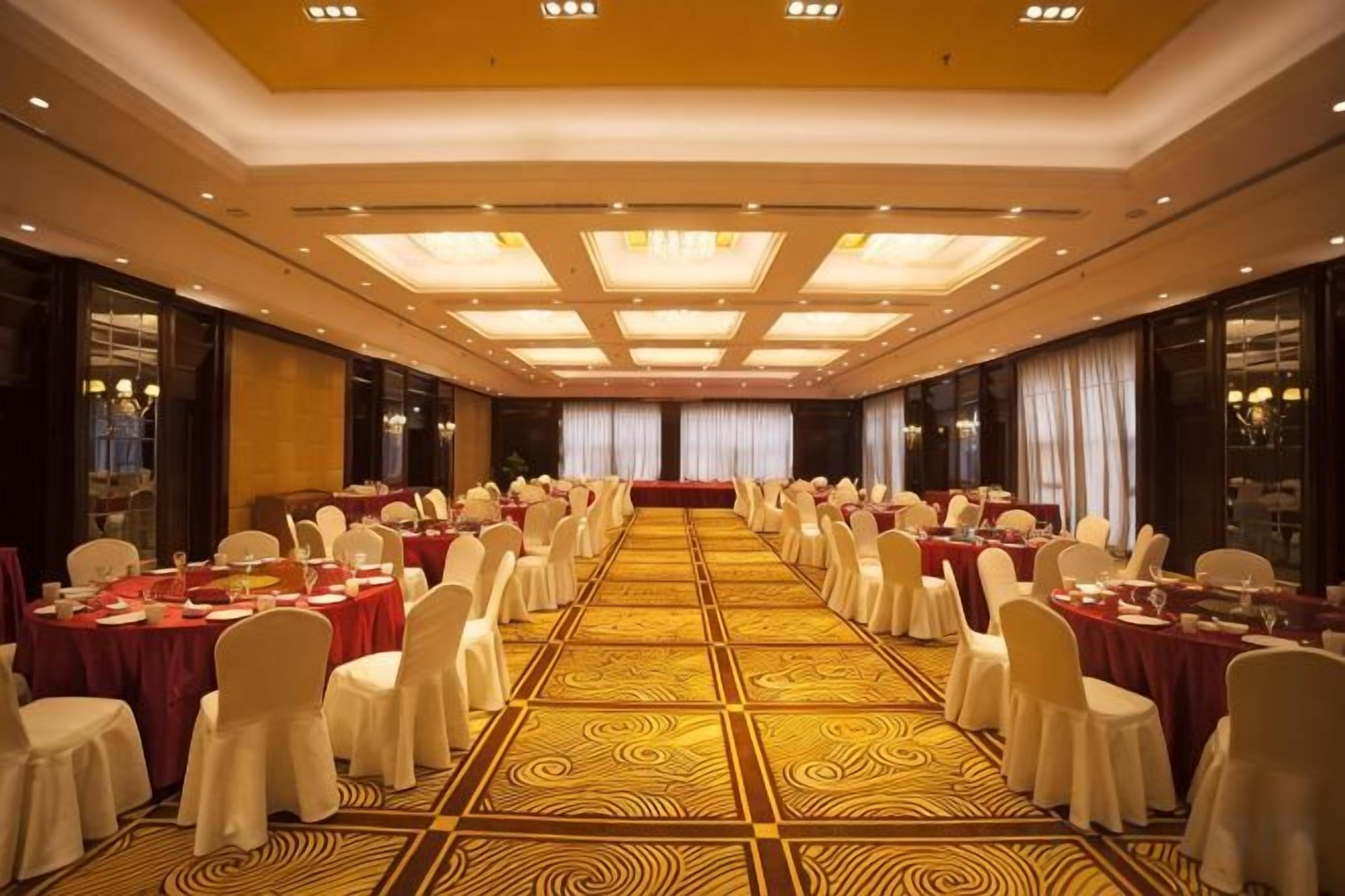 A banquet hall with round tables, chairs, and a patterned carpet.