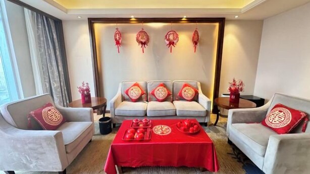 A living room with a sofa set, a coffee table with red tablecloth, and decorative items on the wall. - Blue Horizon Jun Hua Hotel (Fei County)