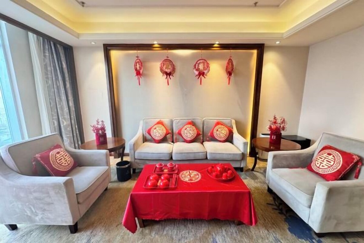 A living room with a sofa set, a coffee table with red tablecloth, and decorative items on the wall.