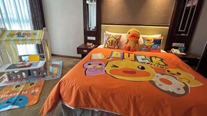 A hotel room with a bed featuring a colorful bedspread with cartoon duck characters. There is a small table with a toy duck and a chair. - Blue Horizon Jun Hua Hotel (Fei County)