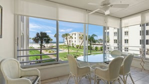 A balcony with a glass table and wicker chairs, overlooking a pool and palm trees. - Island House Beach Resort 12S (Sarasota)
