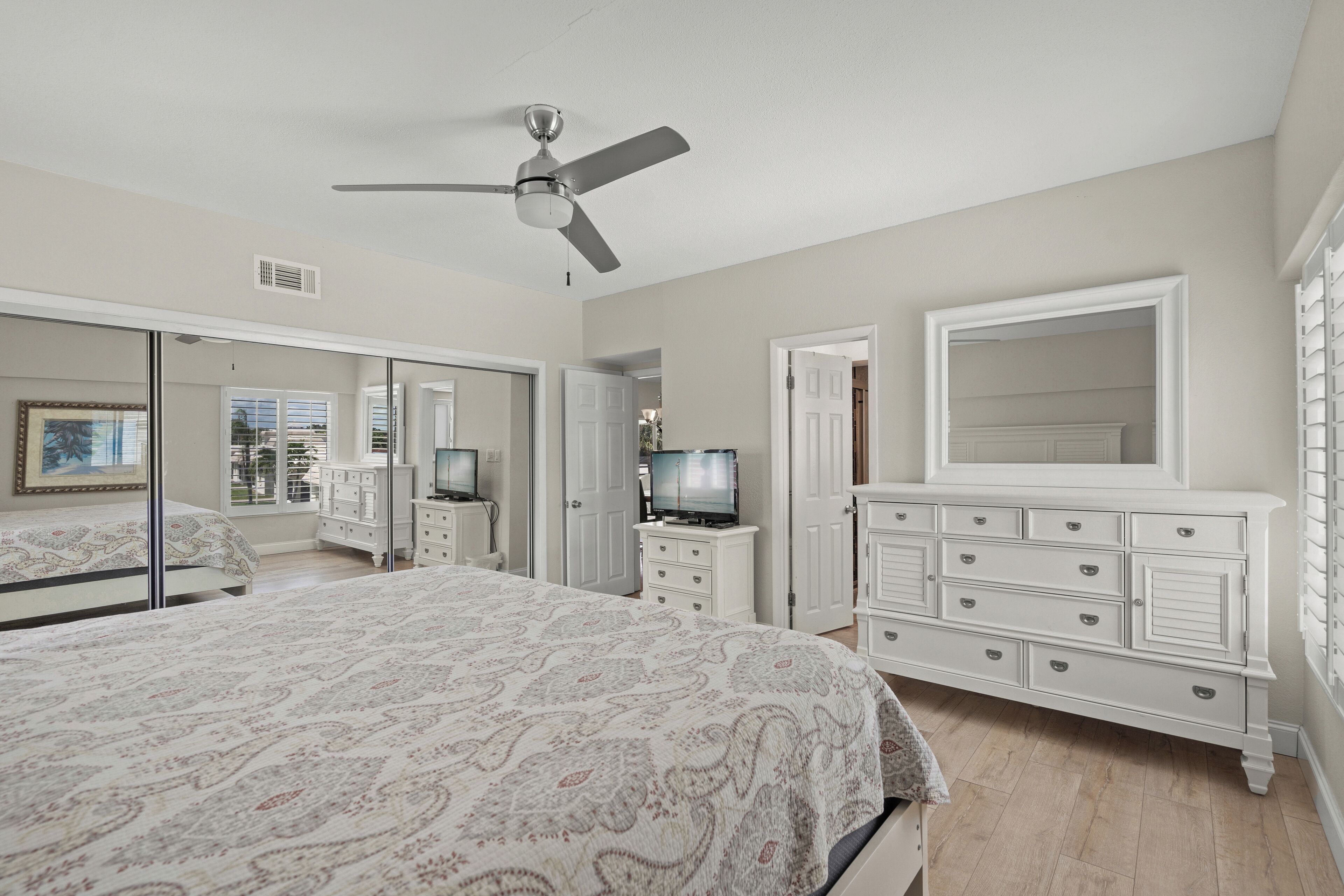 Ein Schlafzimmer mit Bett, Kommode, Fernseher und Deckenventilator.
