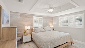 Une chambre à coucher avec une tête de lit en bois, un lit avec une literie blanche, deux tables de chevet avec des lampes et un ventilateur de plafond.