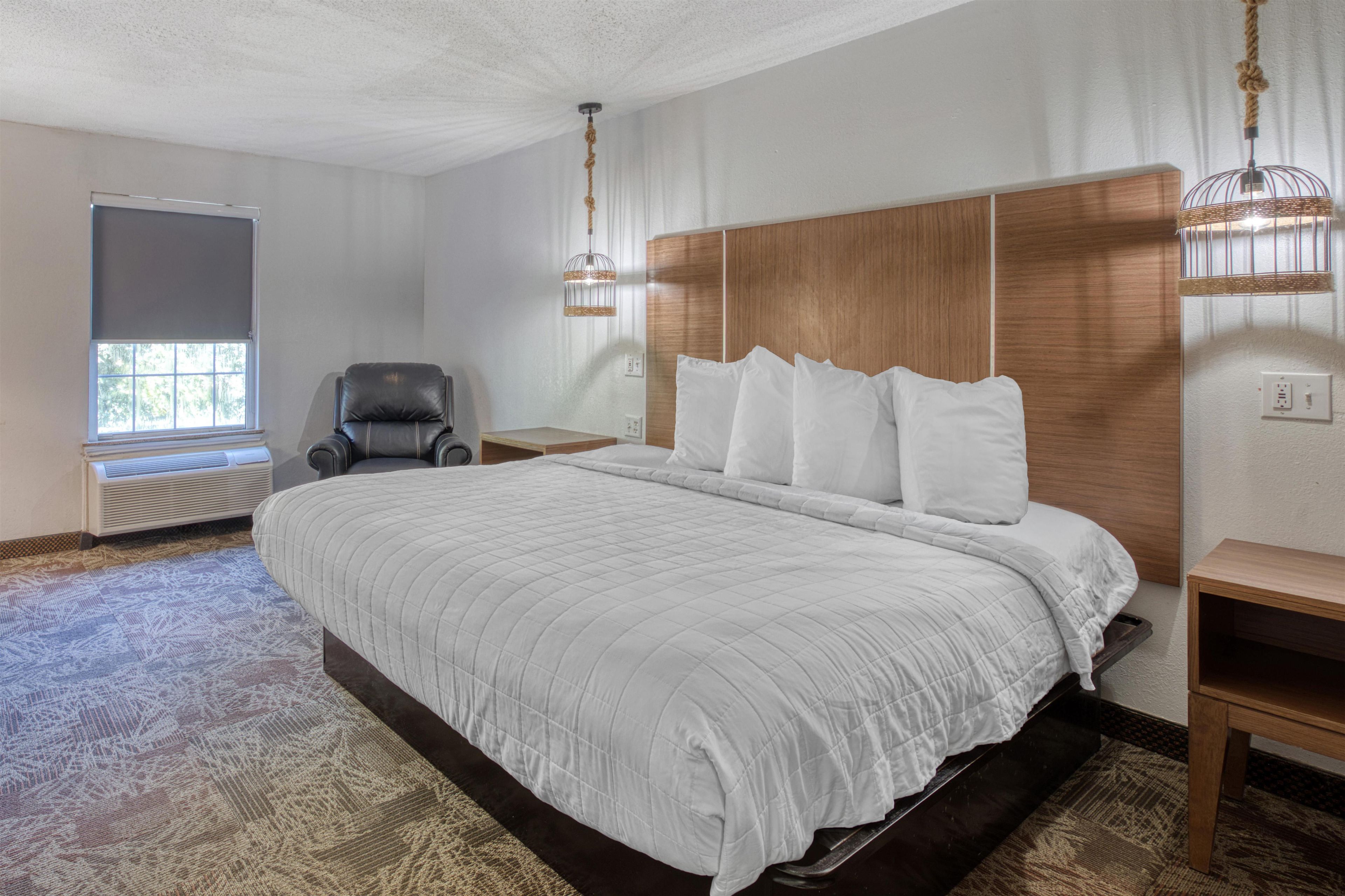 Ein Hotelzimmer mit einem großen Bett, einem Sessel, einem Nachttisch, einem Fenster und einer Deckenleuchte.