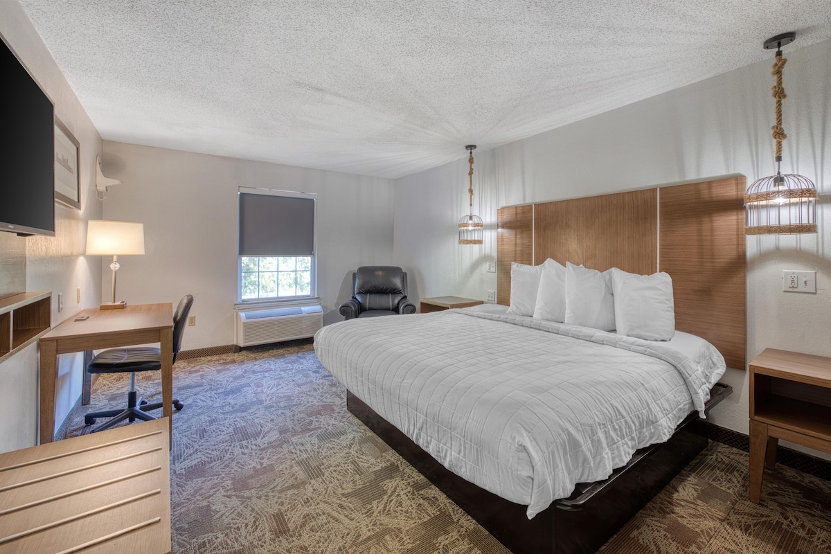 A hotel room with a large bed, a desk with a chair, a television, and a window with blinds.