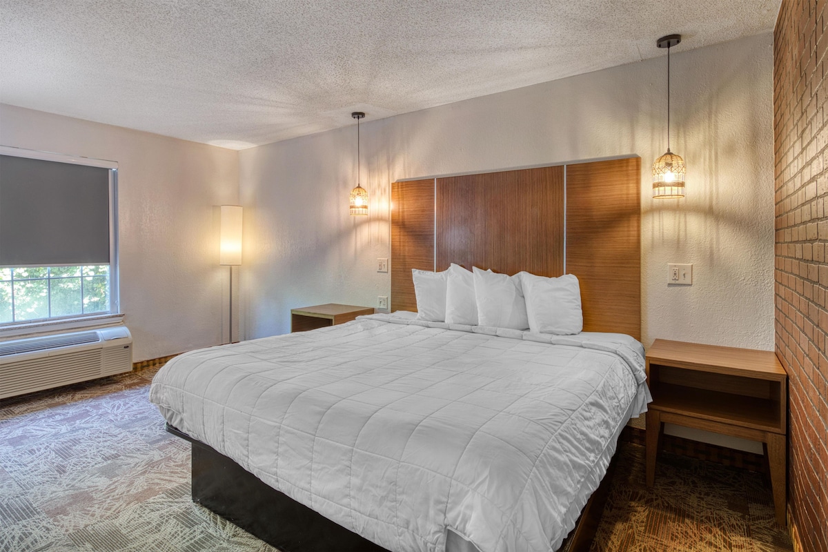 A hotel room with a large bed, bedside tables, a heater, and a window with a view.