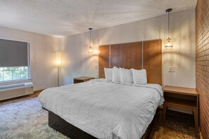 A hotel room with a large bed, bedside tables, a heater, a window with a view, and a brick wall. - SureStay Hotel by Best Western Tuscaloosa Southeast (Tuscaloosa)