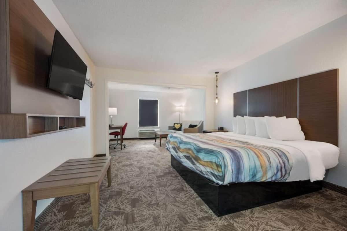 A hotel room with a bed, a desk, a chair, a TV, and a window.