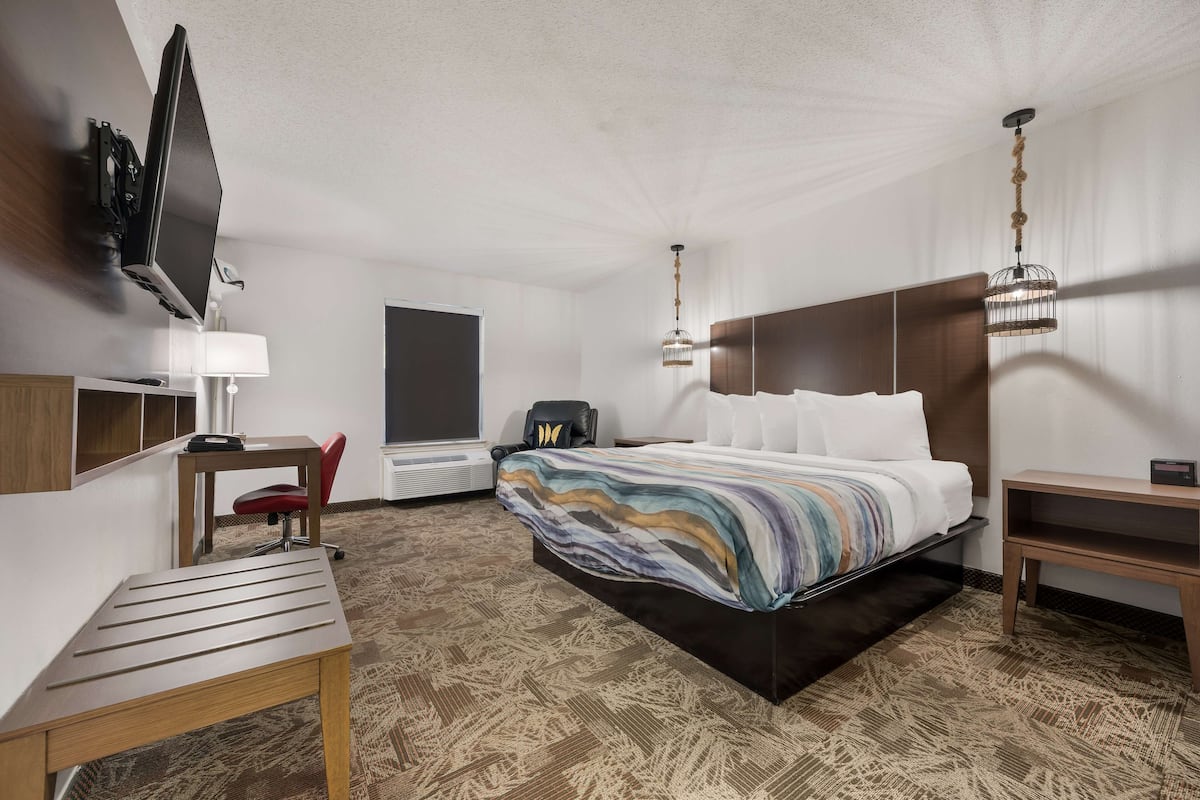 A hotel room with a bed, a desk, a chair, a TV, and a lamp.