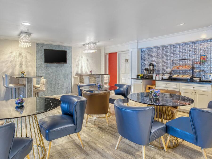 A modern hotel room with a dining area, a kitchen, and a TV mounted on the wall.