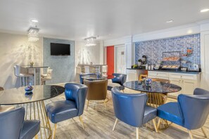 Moderni hotellihuone, jossa on ruokailutila, keittiö ja seinälle asennettu televisio.
