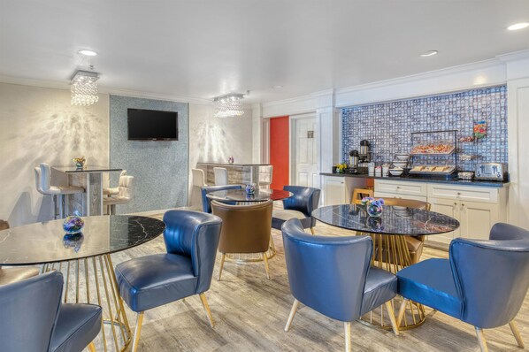 A modern hotel room with a dining area, a kitchen, and a TV mounted on the wall.