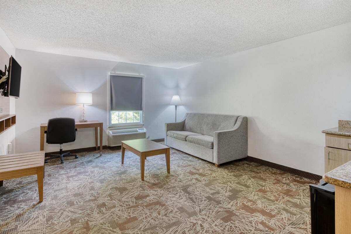 A compact living space with a sofa, a small table, a chair, and a television mounted on the wall.