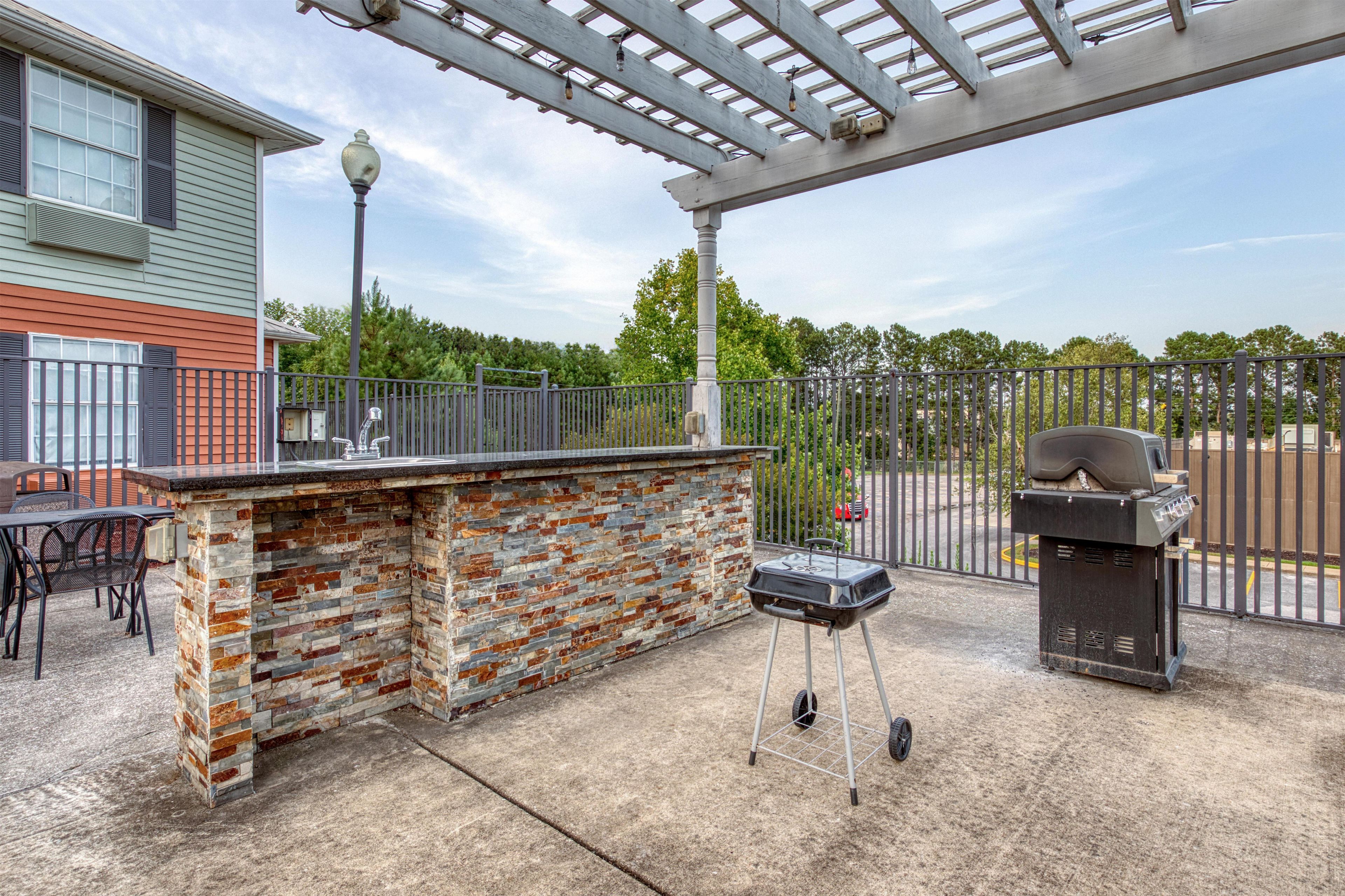 Een terras buiten met een stenen bar, een barbecue en een pergola.