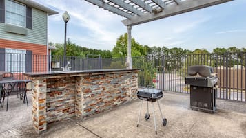 Een terras buiten met een stenen bar, een barbecue en een pergola.