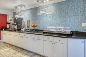 Una cocina con una encimera larga, armarios blancos y un respaldo de mosaico azul.