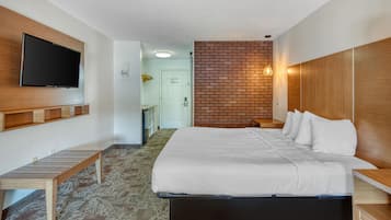 A hotel room with a bed, a TV mounted on the wall, a wooden bench, and a brick accent wall.