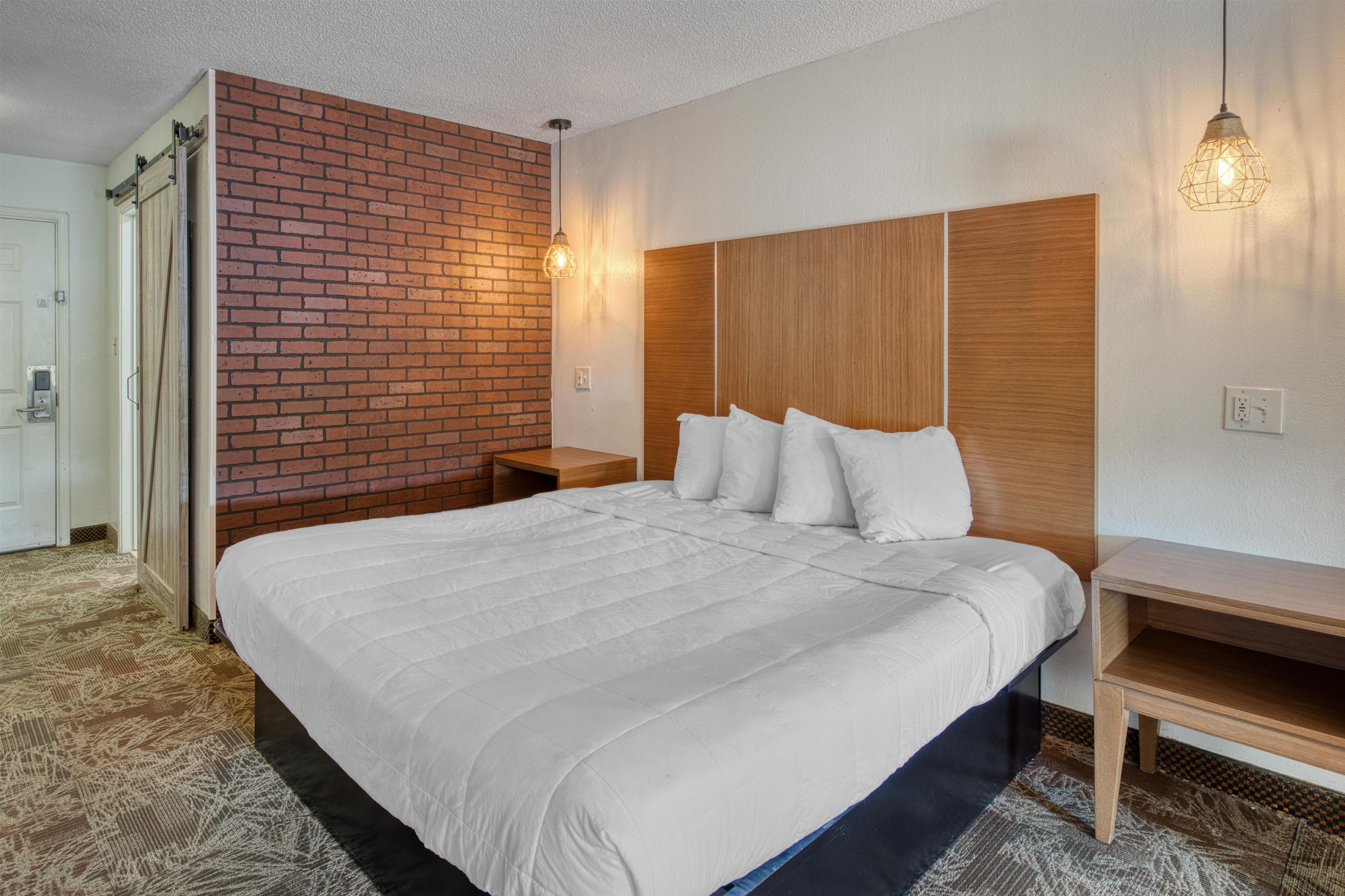 Habitación de hotel con una cama grande, cabecera de madera, pared decorativa de ladrillo y una lámpara colgante.