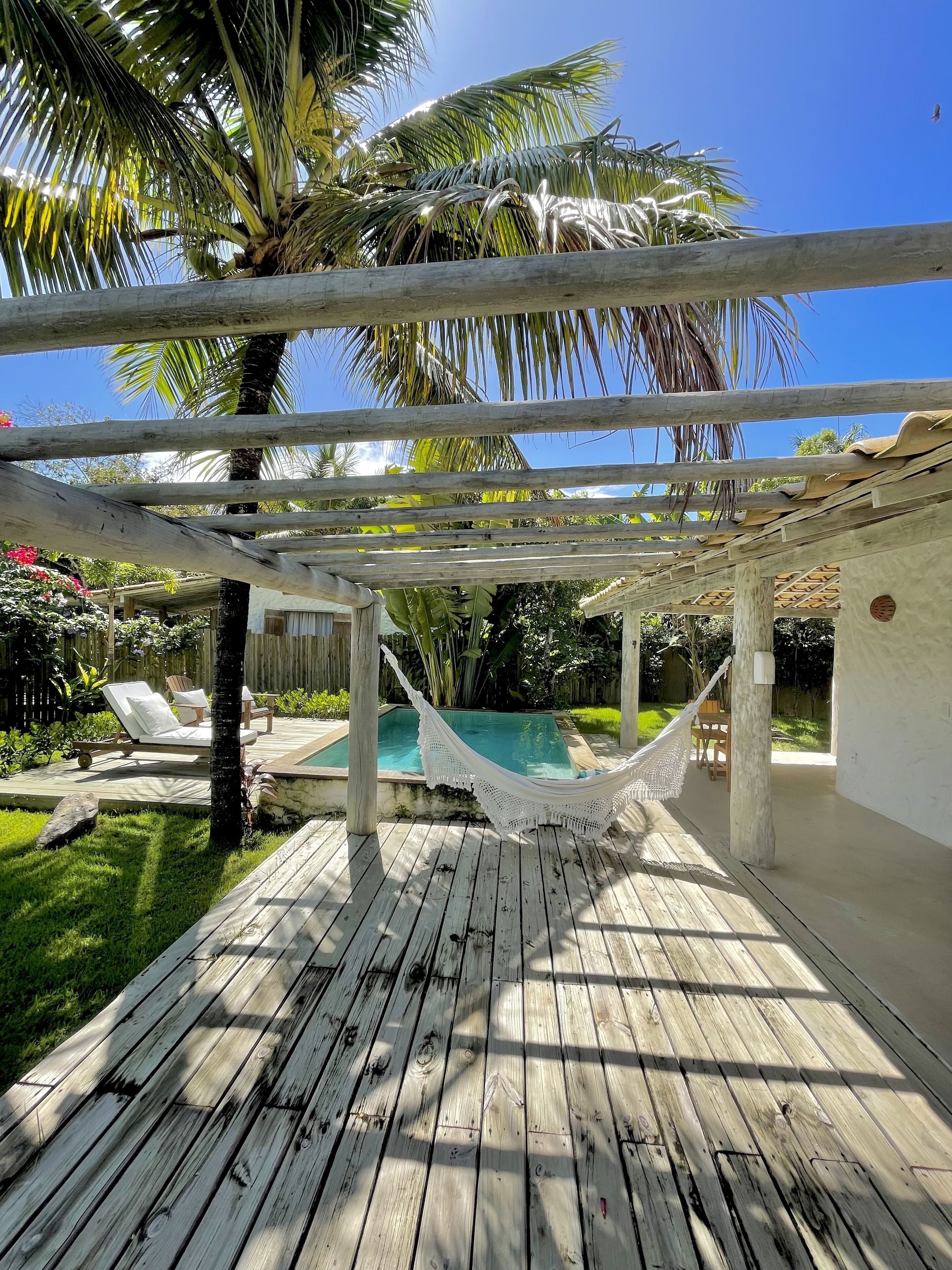 Una terraza de madera con una hamaca, una piscina y un porche de madera.