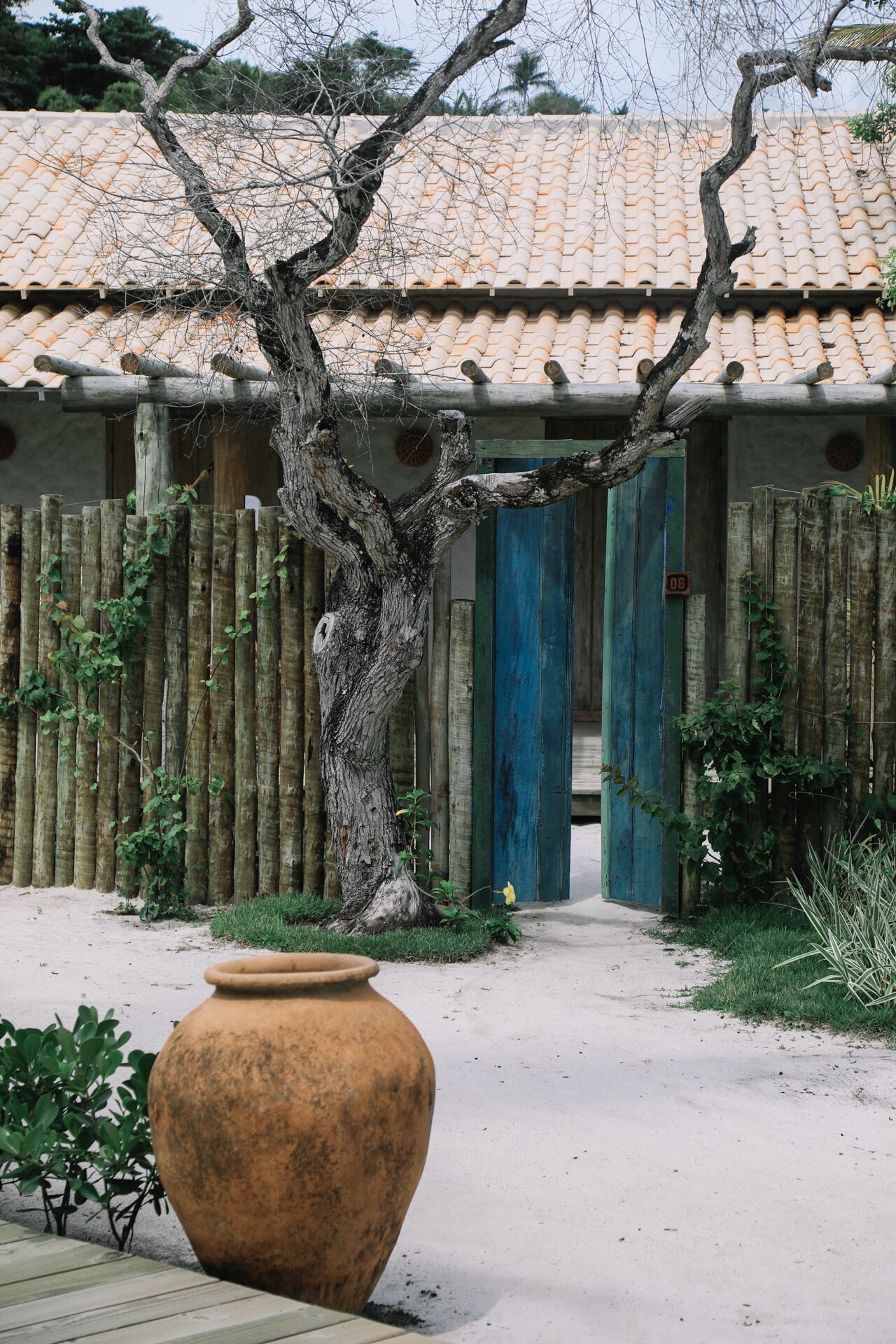 Un bâtiment traditionnel avec un toit en tuiles, une clôture en bois et un grand pot en argile au premier plan.