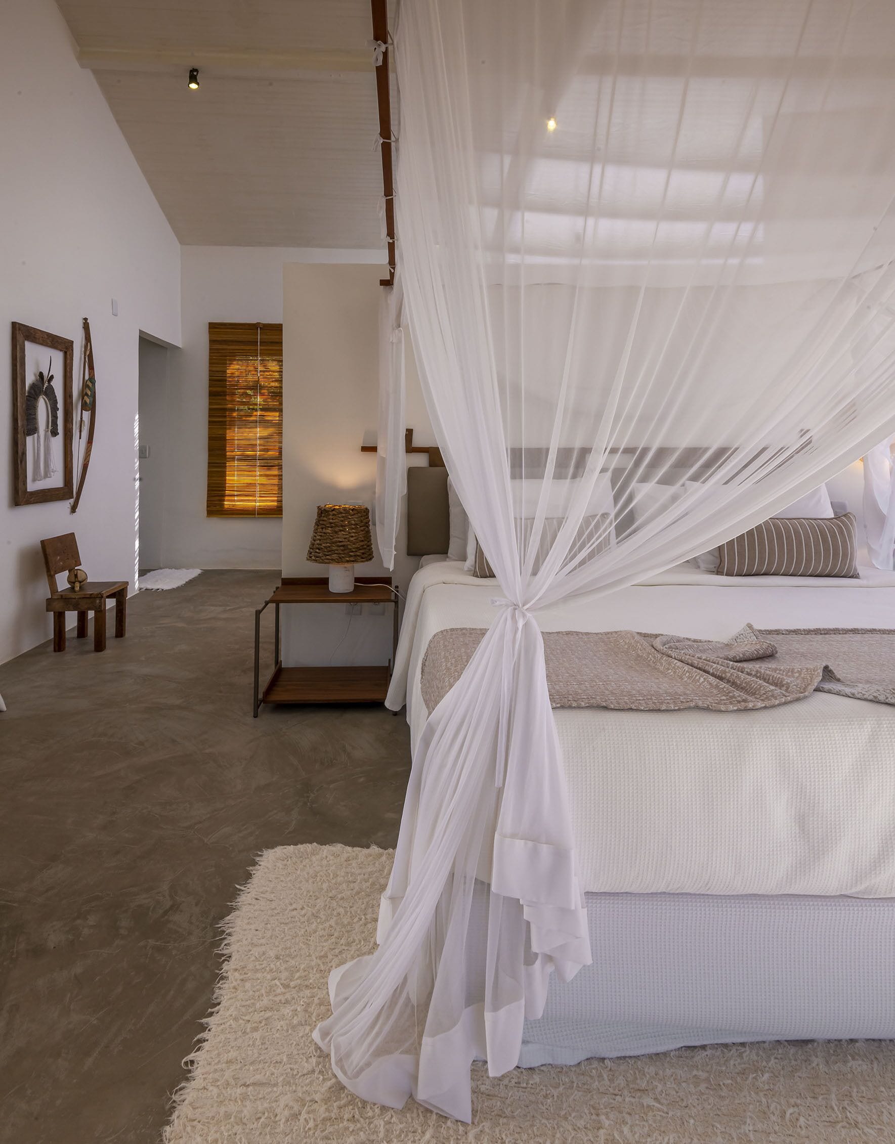 A bedroom with a bed covered by a white canopy, a wooden nightstand with a lamp, and a framed picture on the wall.