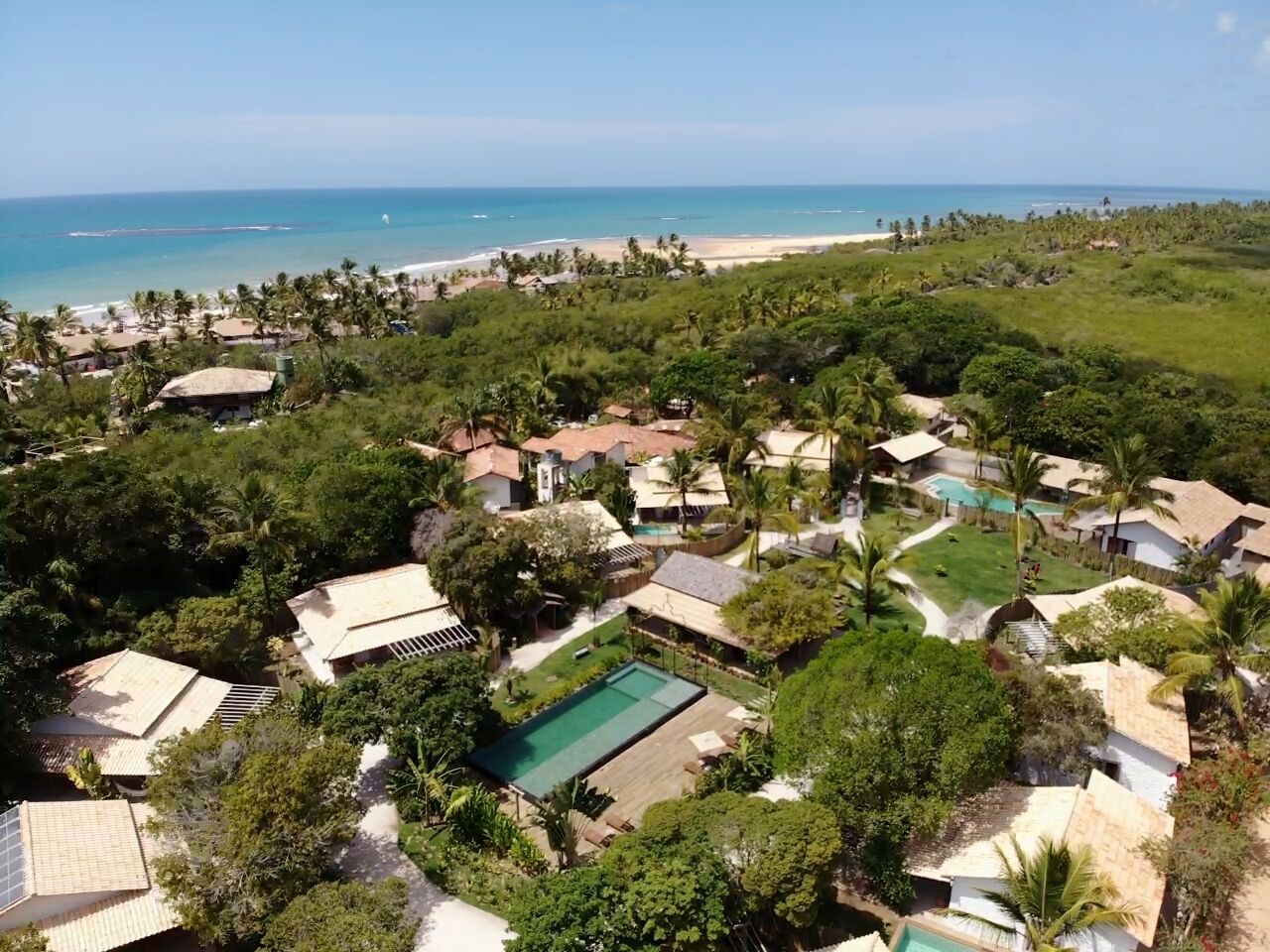 A residential area with houses, a swimming pool, and a beach in the background.
