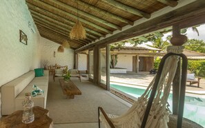 A spacious room with a large window, a hammock, a pool, and a wooden ceiling.