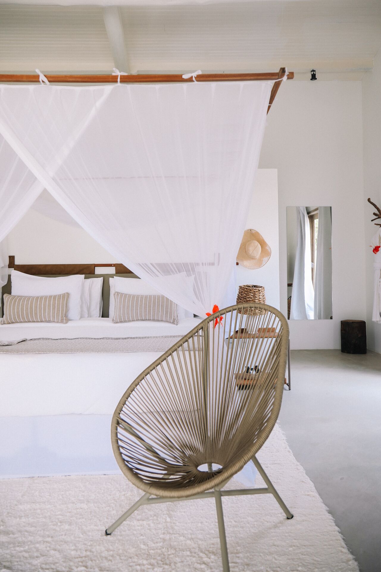 A bedroom with a canopy bed, a rattan chair, and a large mirror.