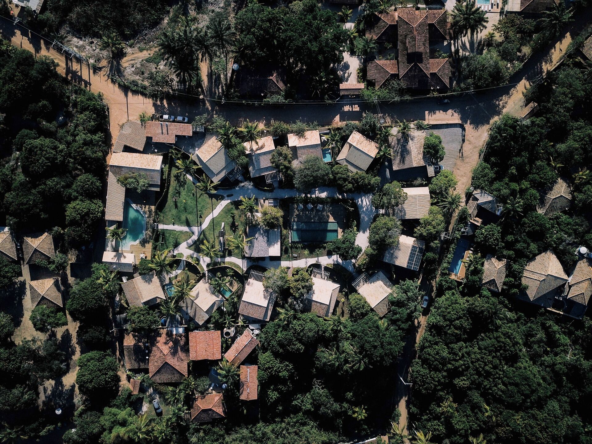 An aerial view of a residential area with multiple houses, a central swimming pool, and surrounding greenery.
