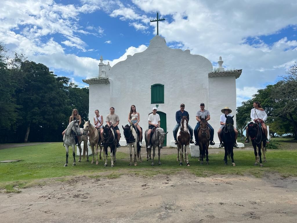 A group of people on horses in front of a white church with a cross on top.