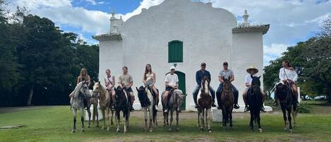 A group of people on horses in front of a white church with a cross on top.