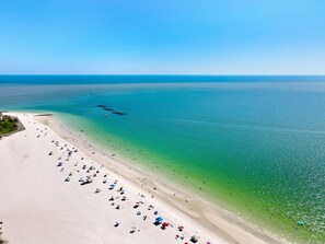 Une plage à l’eau turquoise et limpide, avec un rivage sablonneux et plusieurs parasols.