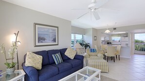 A living room with a blue sofa, a glass coffee table, and a dining area with chairs and a table.