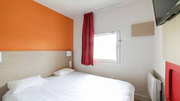 Habitación de hotel con cama, ventana con cortinas rojas, televisor montado en la pared y radiador.