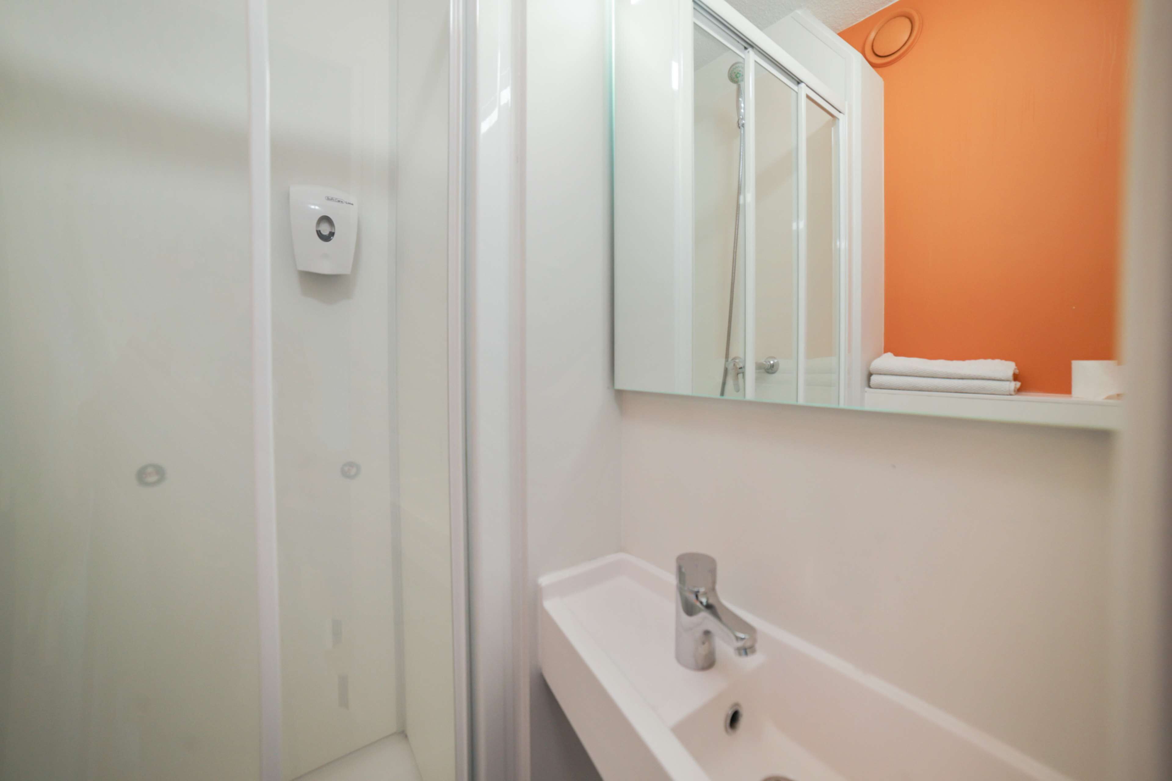 Een badkamer met een douche, wastafel en spiegel.