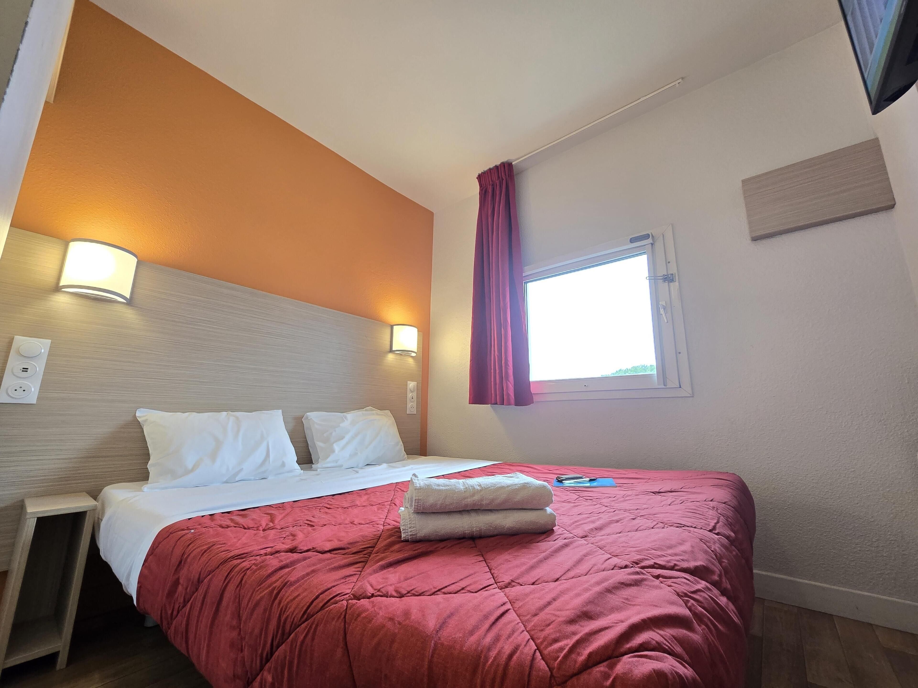 Habitación de hotel con cama, mesitas de noche, ventana con cortinas e iluminación en la pared.