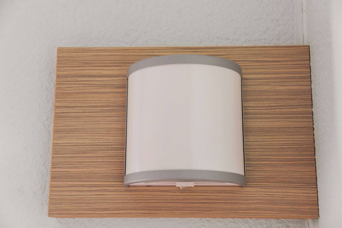 A wall-mounted light fixture with a cylindrical shape and a metallic trim, set in a wooden panel frame.