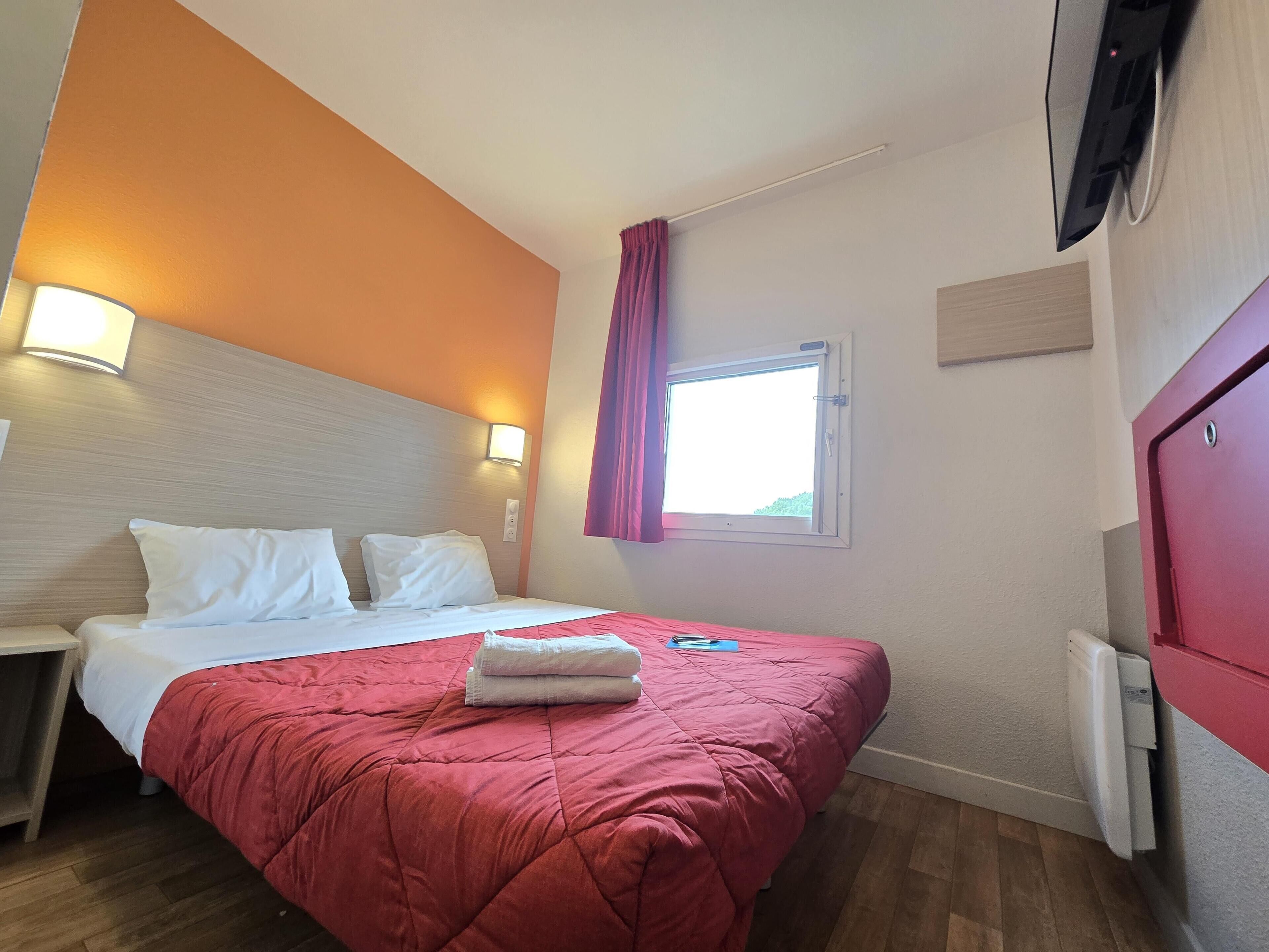 Hotelkamer met een bed, nachtkastje, raam met gordijnen en een aan de muur bevestigde televisie.