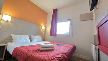 Une chambre d’hôtel avec un lit, une table de chevet, une fenêtre avec des rideaux et un téléviseur fixé au mur.