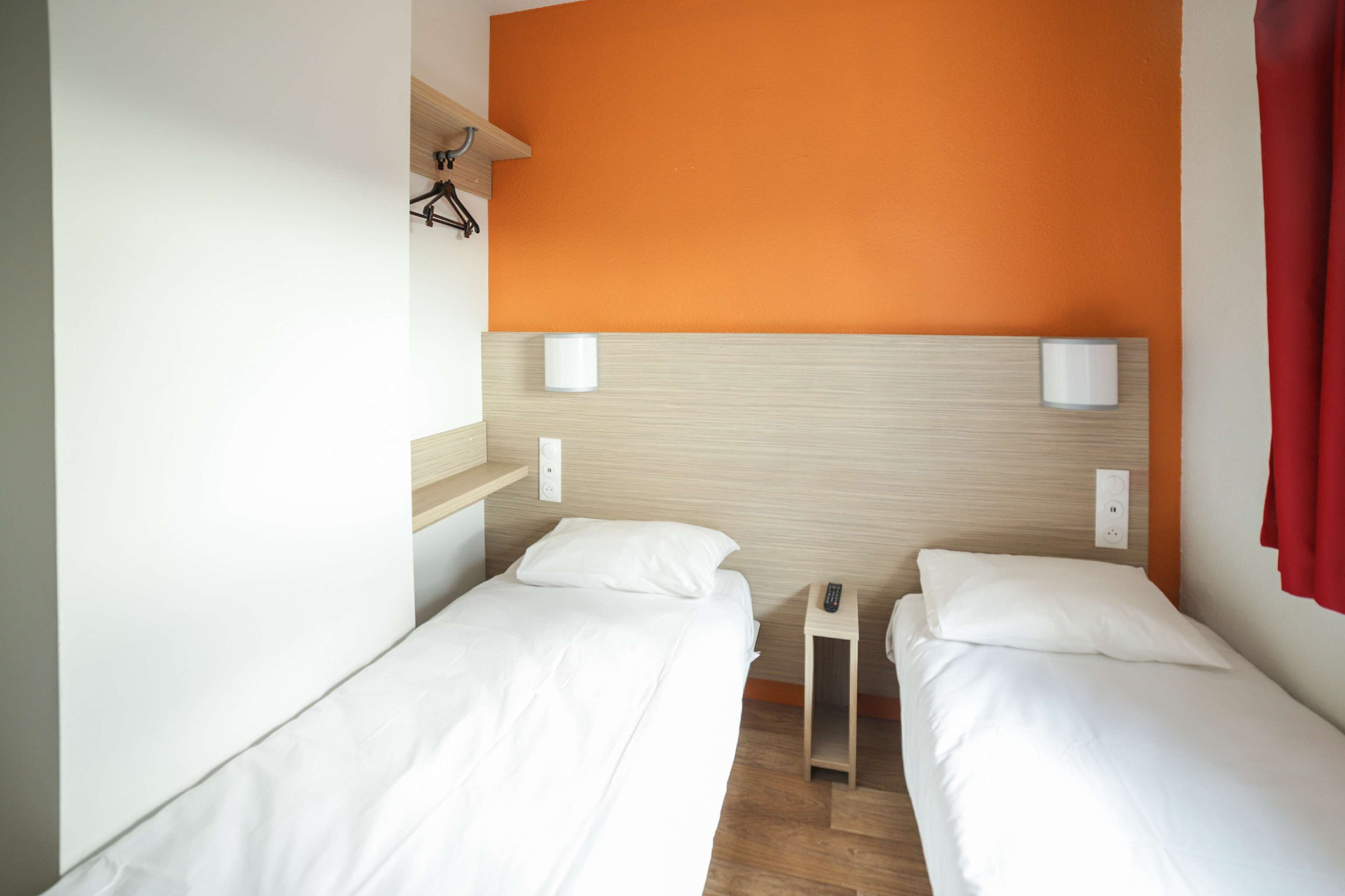 A hotel room with two single beds, a wooden headboard, and a red curtain.