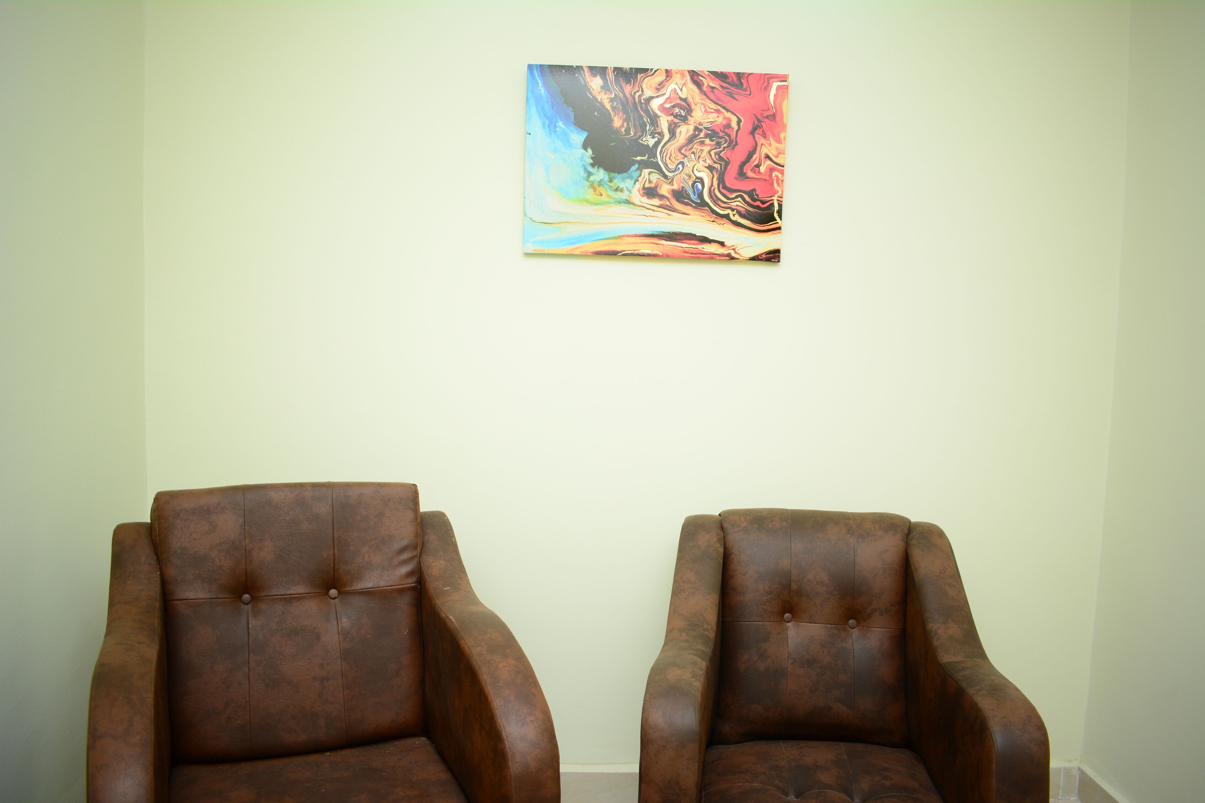 Two brown leather armchairs facing each other with a colorful abstract painting on the wall.