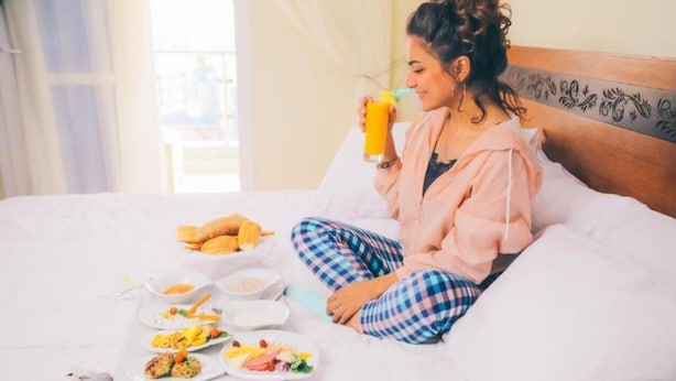 Una persona sentada en una cama con alimentos para el desayuno y una bebida.