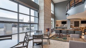 A spacious indoor area with a large dining table, multiple chairs, a fireplace, and a kitchen area with a bar. - Cambria Hotel Louisville Downtown-Whiskey Row (Louisville)