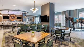 A modern dining area with a bar, green upholstered chairs, and a large horse statue.